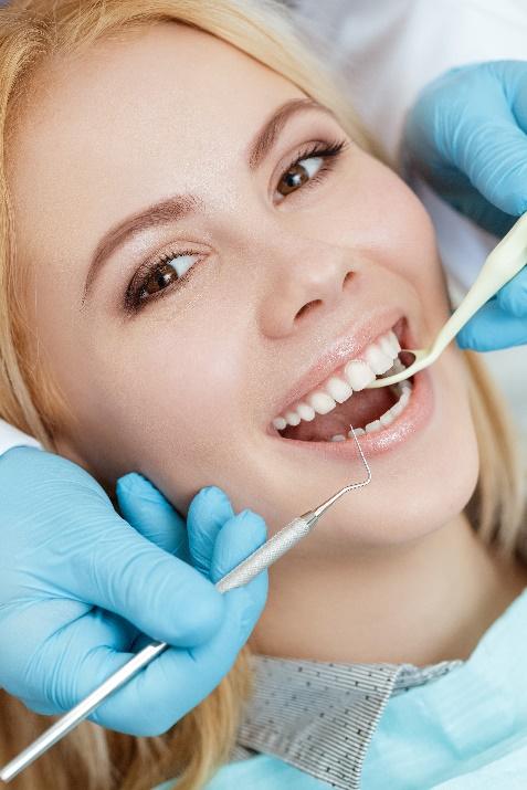Woman receiving dental examination from dentist wearing blue gloves in clinical setting.