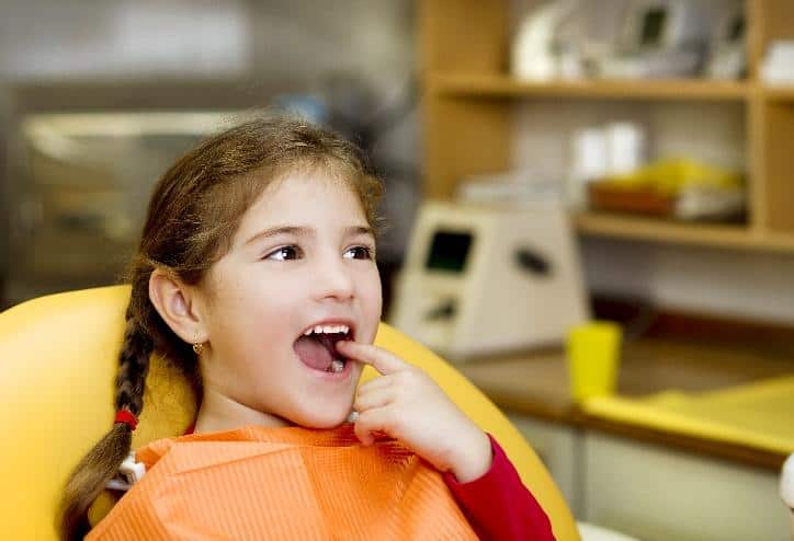 Young girl smiling in dental chair wearing orange bib at pediatric dental office.