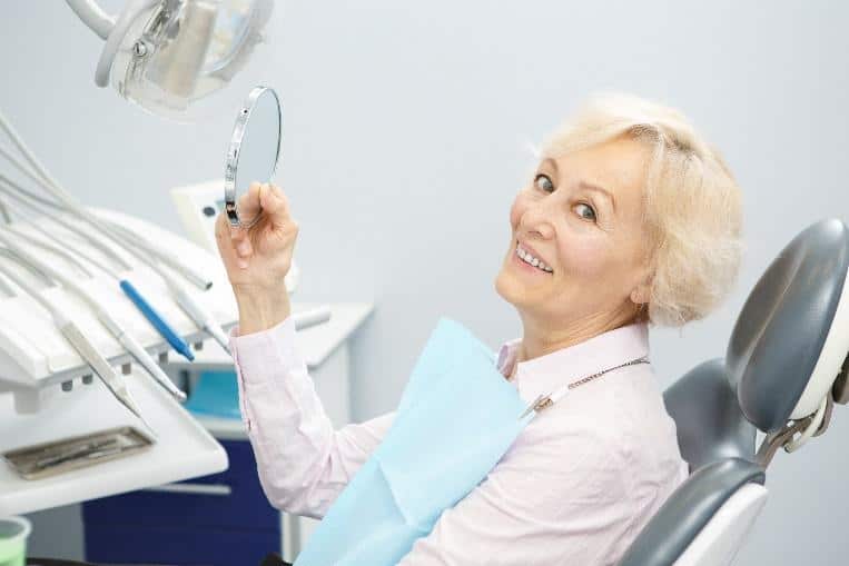 Senior woman dentist examining dental mirror in modern dental office treatment room