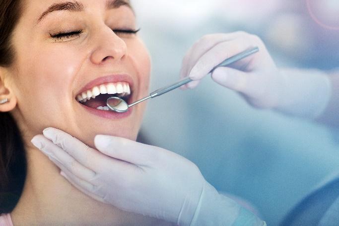 Woman smiling during dental examination with dentist using mirror and explorer tool.