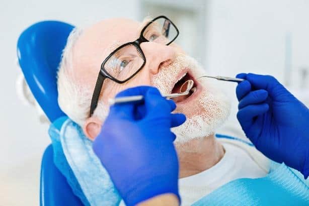 Dentist in blue gloves examining patient's teeth during dental procedure in clinical setting.