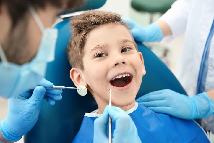 Young boy smiling during dental examination with dentist in blue gloves and protective gear.