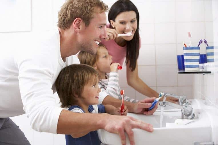 Family of four brushing teeth together at bathroom sink during dental hygiene routine.