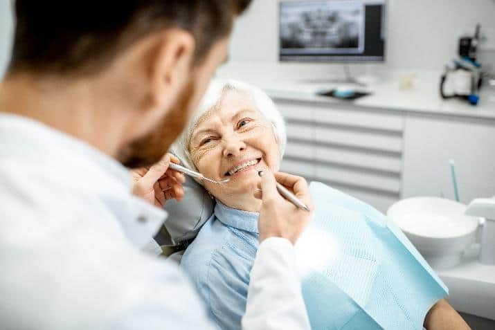 Dentist examining senior patient's teeth in modern dental office treatment chair