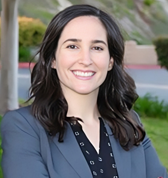 Professional woman smiling at camera wearing blue blazer in outdoor dental office setting.