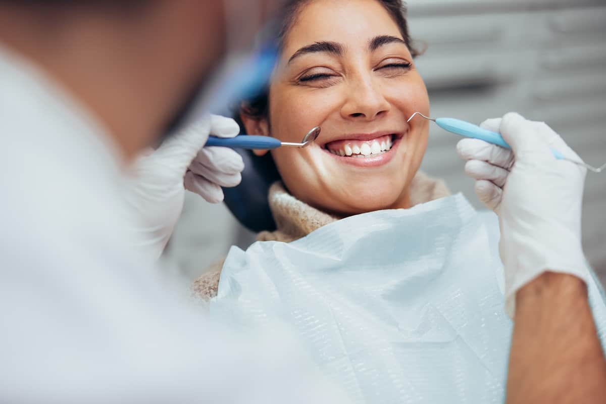 Dentist examining smiling female patient in dental office setting with gloved hands.