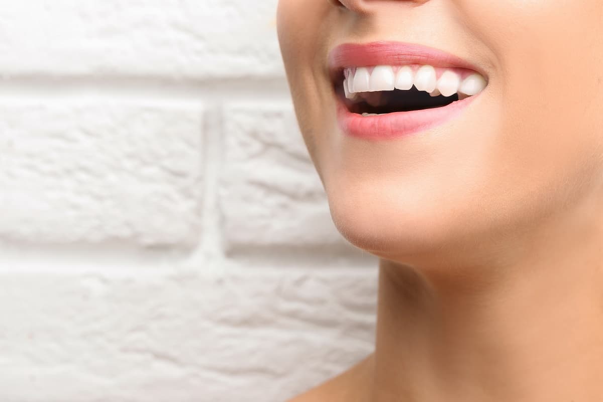 Woman smiling brightly against white brick background, showcasing healthy white teeth.