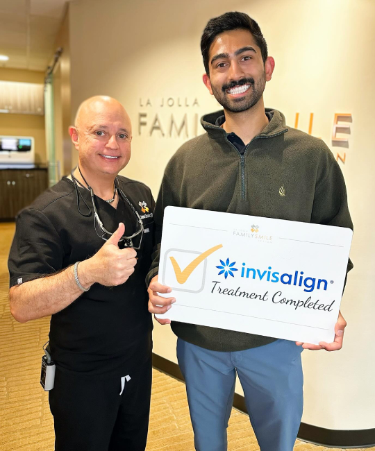 Two men holding Invisalign treatment completion certificate in dental office setting.