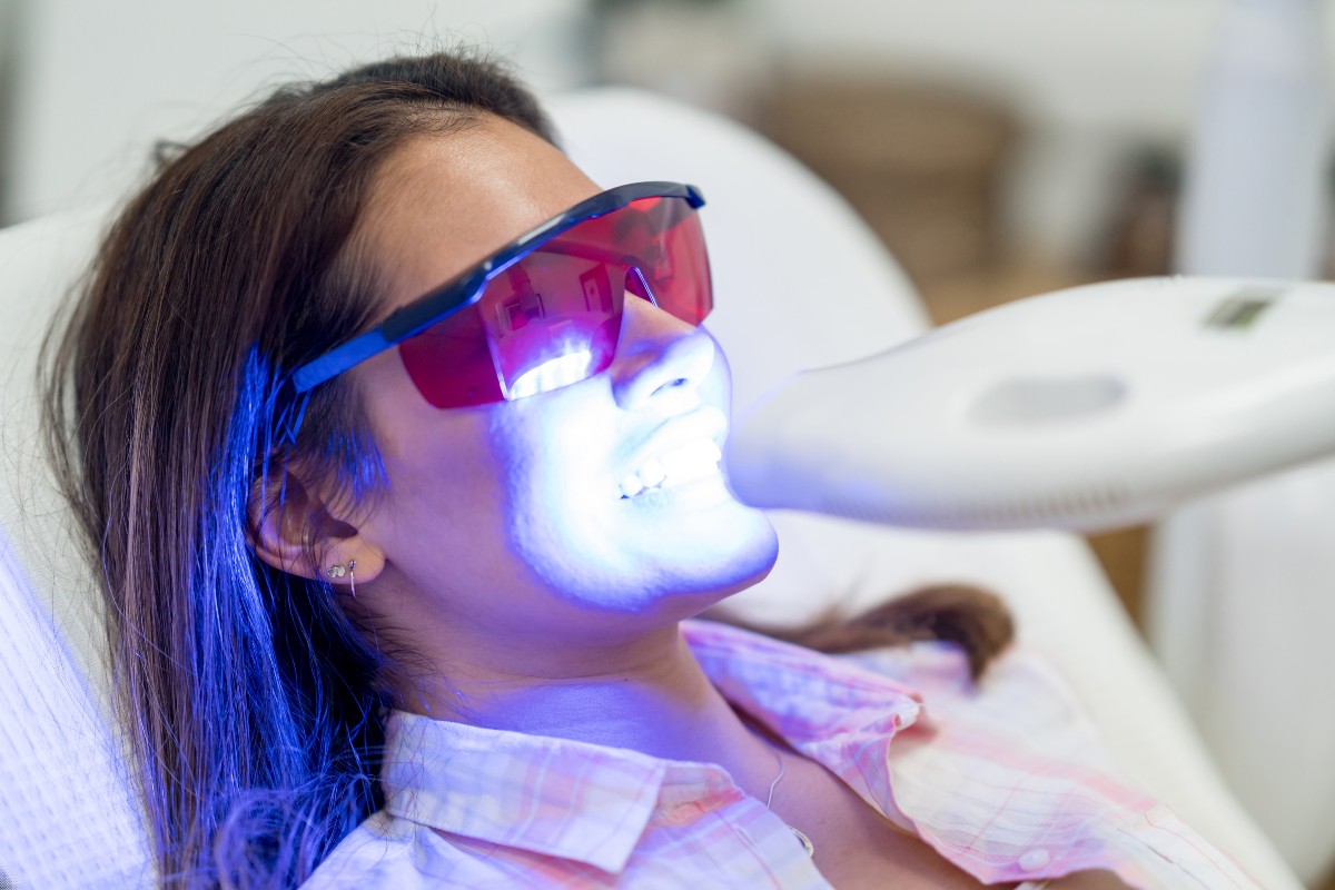 Woman receiving professional teeth whitening treatment with blue LED light in dental office.