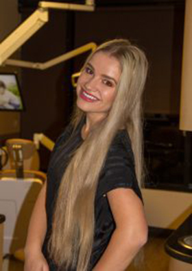 Woman with long blonde hair smiling at camera in dental office setting.