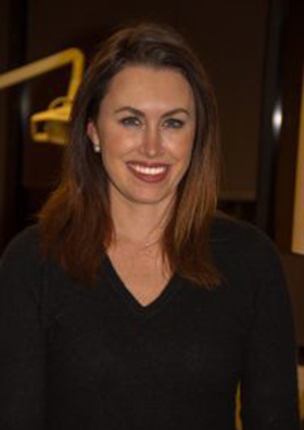 Woman with long brown hair smiling at camera in professional dental office setting.