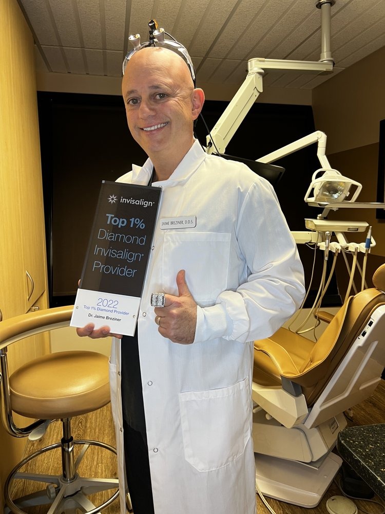 Dentist in white coat giving thumbs up in modern dental office treatment room.