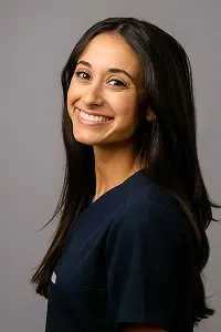Professional headshot of a smiling woman with long dark hair wearing a dark blue top against a gray background.