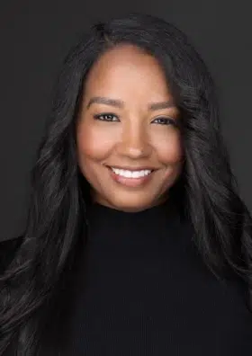 Professional headshot of smiling woman with long dark hair against dark background for dental practice.