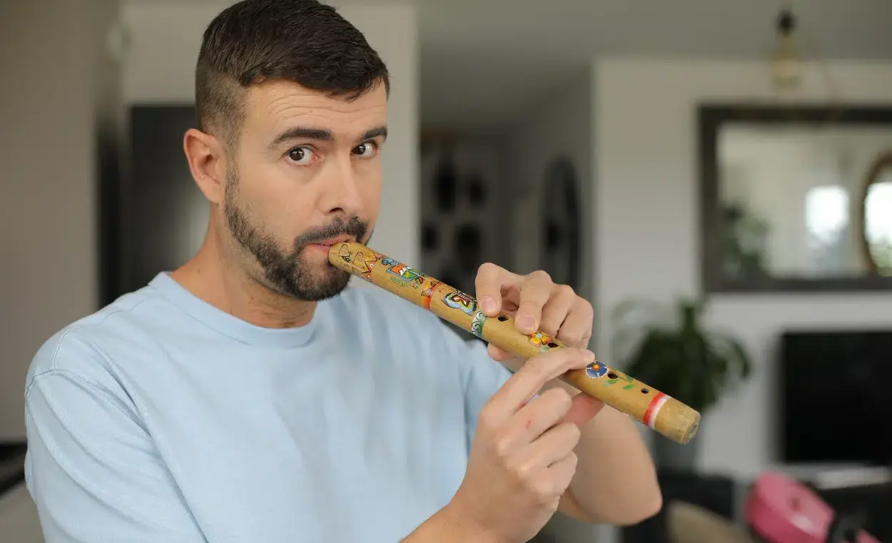 Man playing wooden flute with colorful decorative bands indoors.
