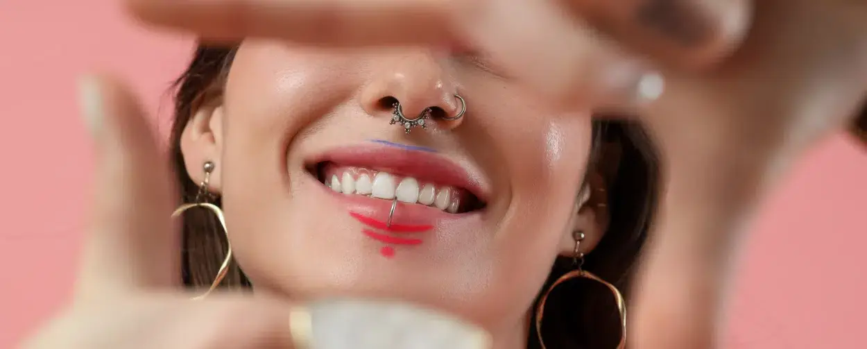 Close-up of a smiling patient with nose and lip piercings wearing clear aligner trays.
